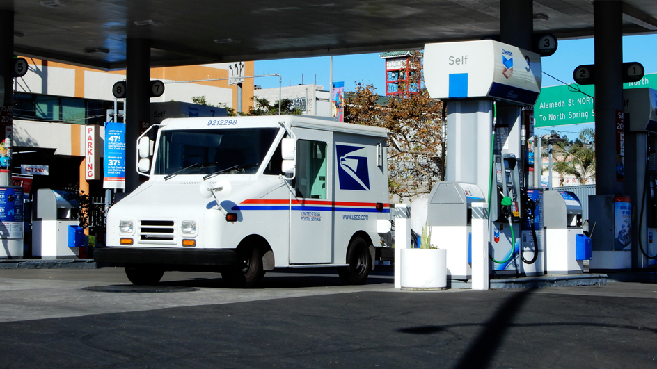 A USPS delivery vehicle is parked near a gas station pump