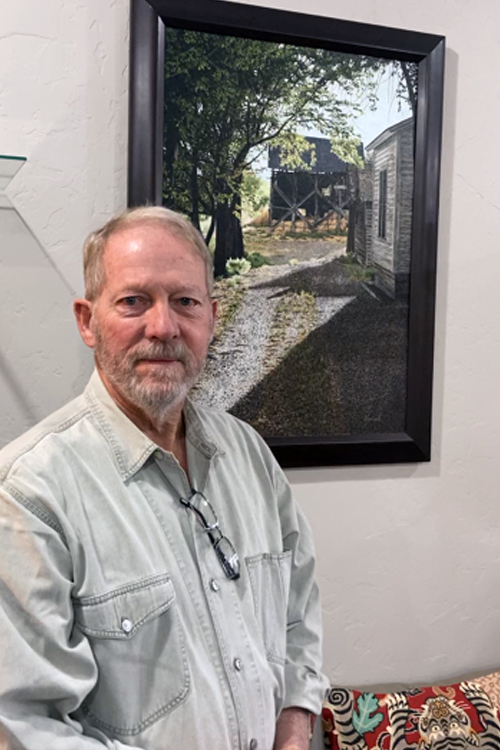 A man in a button-up shirt standing by a painting hanging on a wall