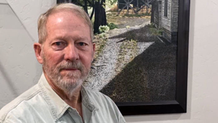 A man in a button-up shirt standing by a painting hanging on a wall