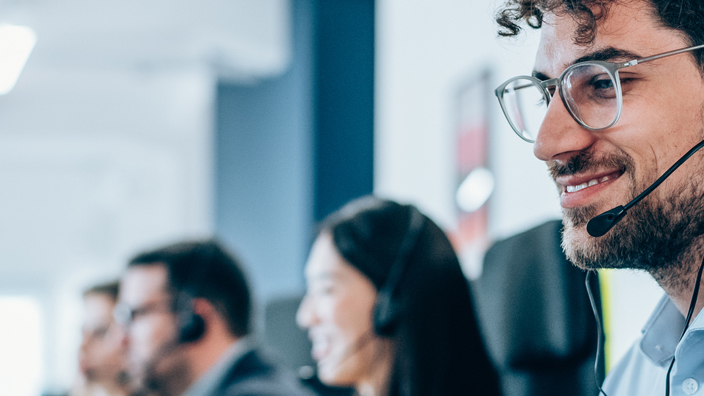 Man in a light-colored shirt sitting at a computer and wearing a headset