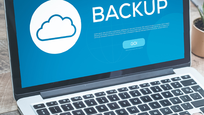 An open laptop computer sitting on a table with the screen displaying the word “backup”