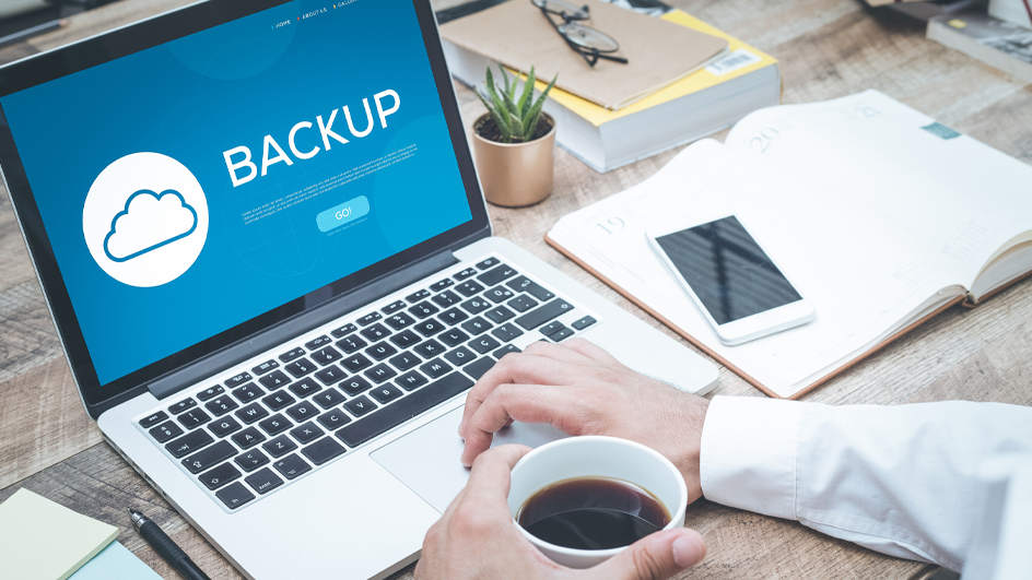 An open laptop computer sitting on a table with the screen displaying the word “backup”