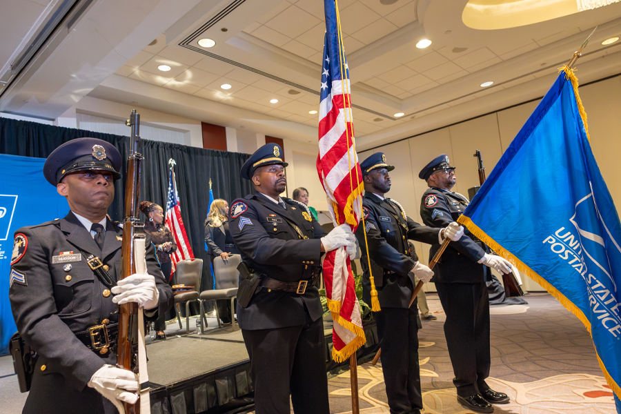 A four-member color guard unit displaying the American flag and a flag displaying the Postal Service logo