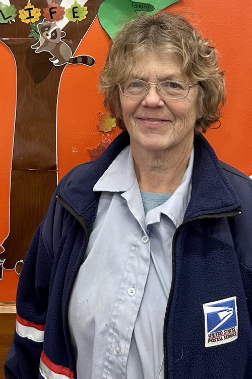 A woman wearing a dark blue jacket with the USPS logo.