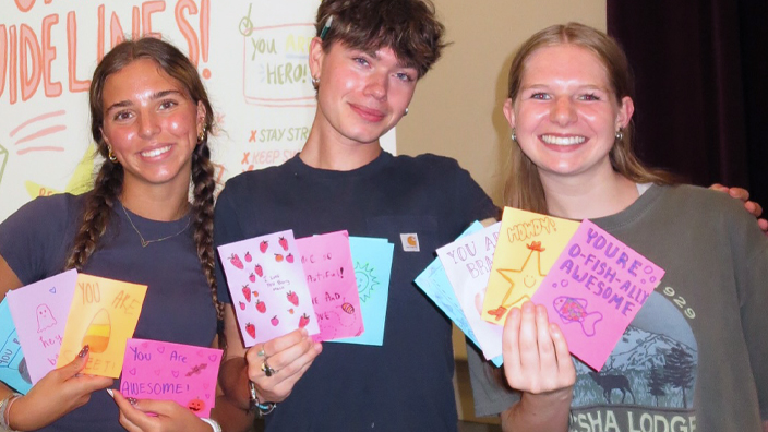 Three people holding up hand-drawn greeting cards