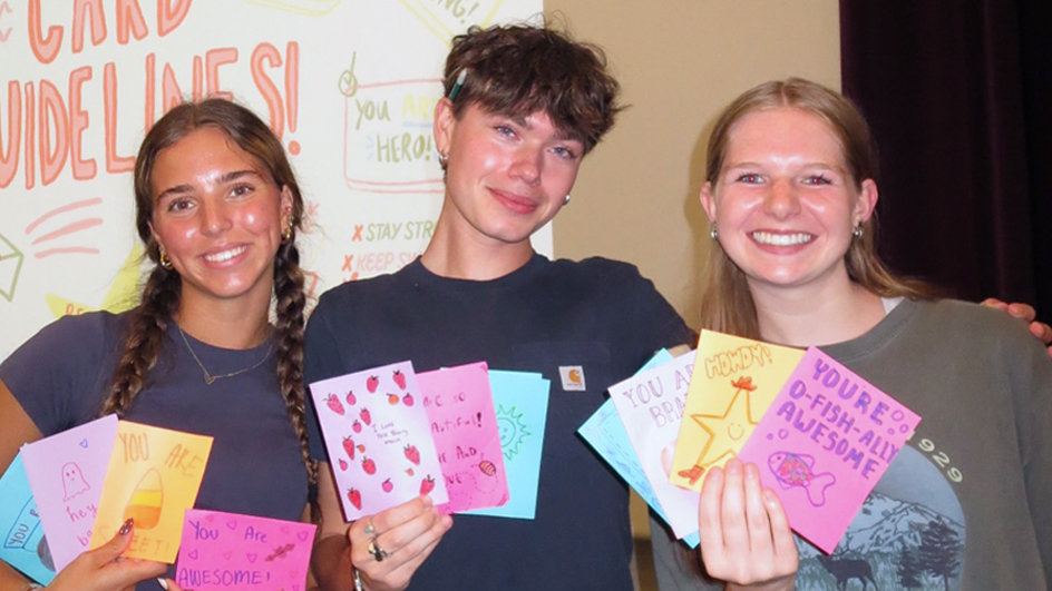 Three people holding up hand-drawn greeting cards