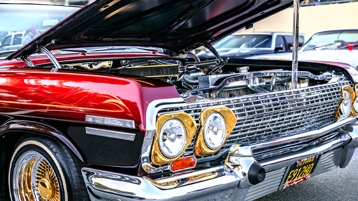 A burgundy Chevrolet Impala with custom pinstriping, chrome trim, gold wire wheels and whitewall tire