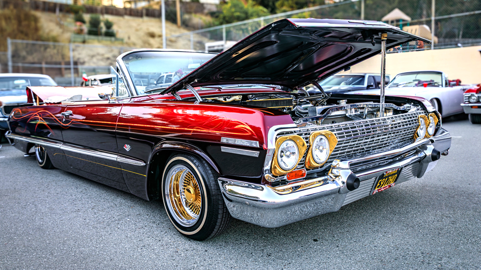 A burgundy Chevrolet Impala with custom pinstriping, chrome trim, gold wire wheels and whitewall tire