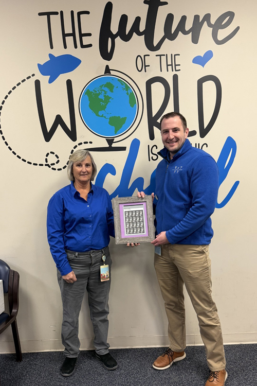 A man and a woman holding up a framed pane of Phillis Wheatley stamps