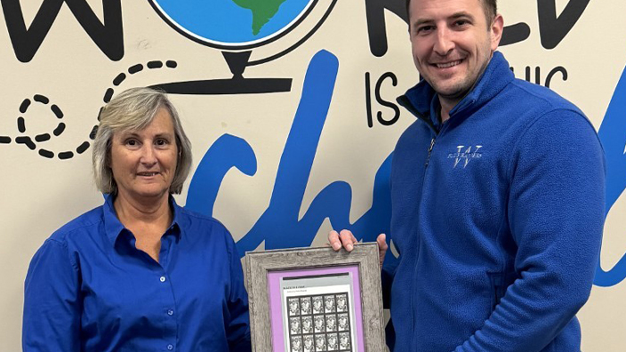A man and a woman holding up a framed pane of Phillis Wheatley stamps