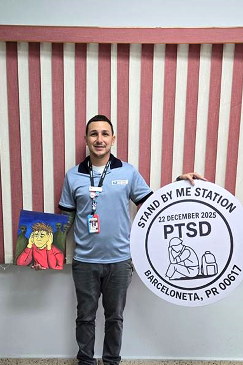 USPS employee wearing a light blue shirt and dark pants and holding an enlargement of a postmark in one hand and a painting in the other