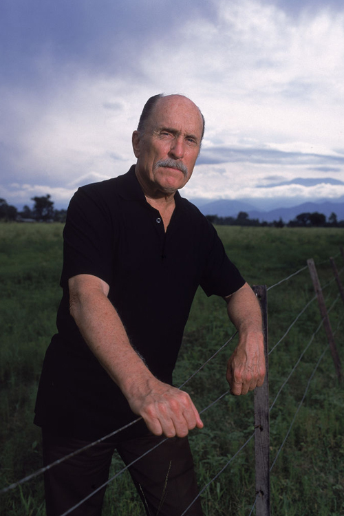 Portrait of American actor Robert Duvall as he rests his arms on a wire fence