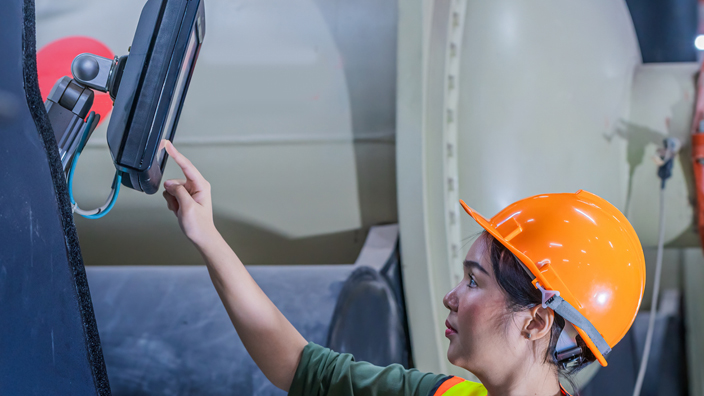 A woman wearing an orange safety vest and hard hat checking an industrial air conditioner