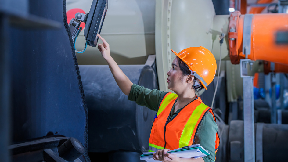 A woman wearing an orange safety vest and hard hat checking an industrial air conditioner