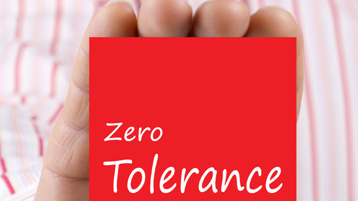 Male hand showing card with text "Zero Tolerance" message. Defocused chart background.