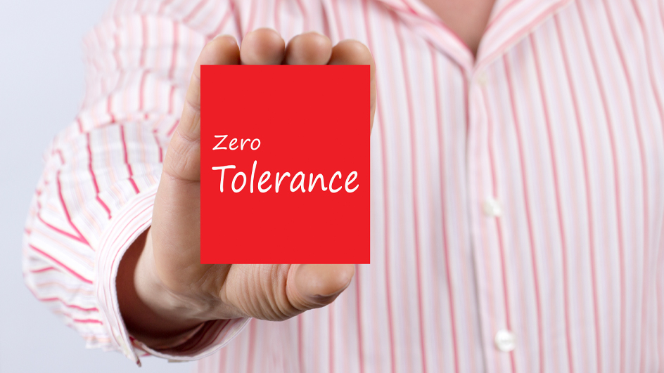 Male hand showing card with text "Zero Tolerance" message. Defocused chart background.
