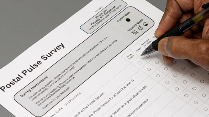 A person holding a clipboard with a paper Postal Pulse survey attached