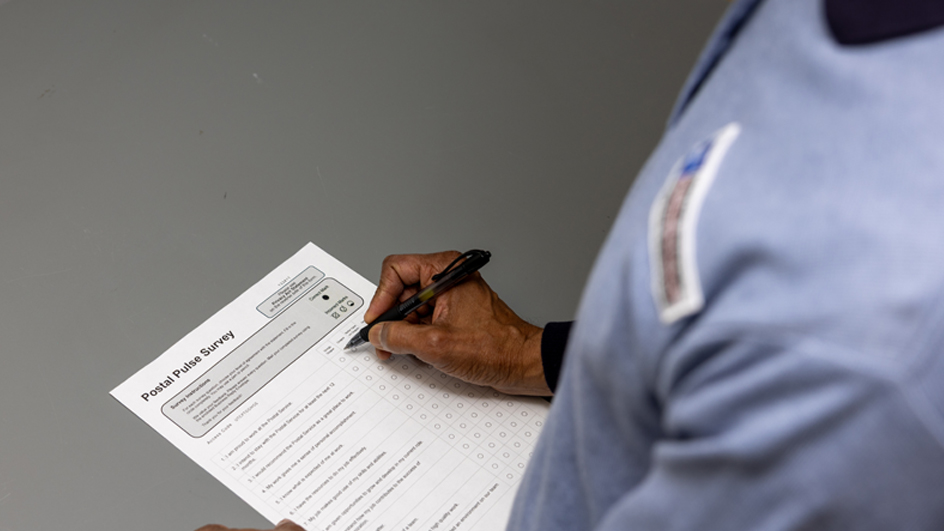 A person holding a clipboard with a paper Postal Pulse survey attached