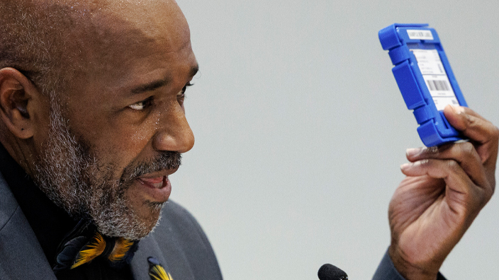 A man behind a podium holding up an audio cartridge