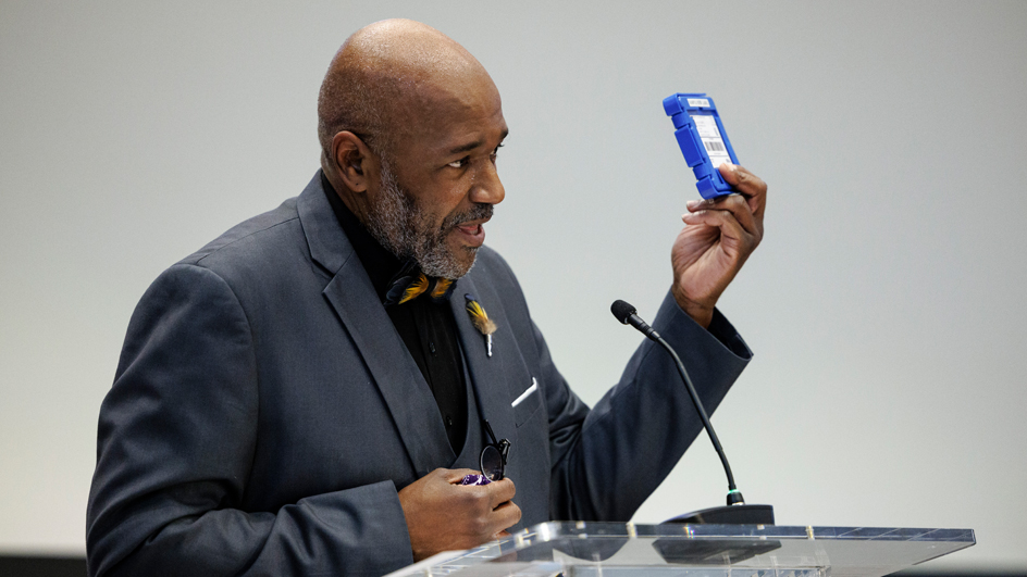 A man behind a podium holding up an audio cartridge