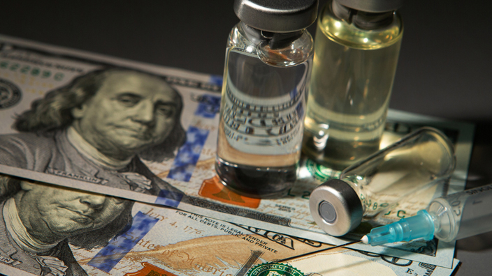 Three medical vials and a hypodermic needle laying on top of two $100 bills