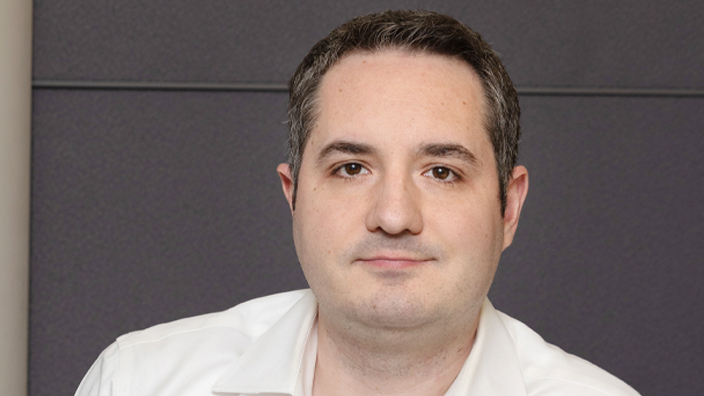 A man wearing a white button-up shirt and sitting down in a chair