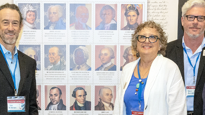 Group standing in front of a large display of Figures of the American Revolution stamps
