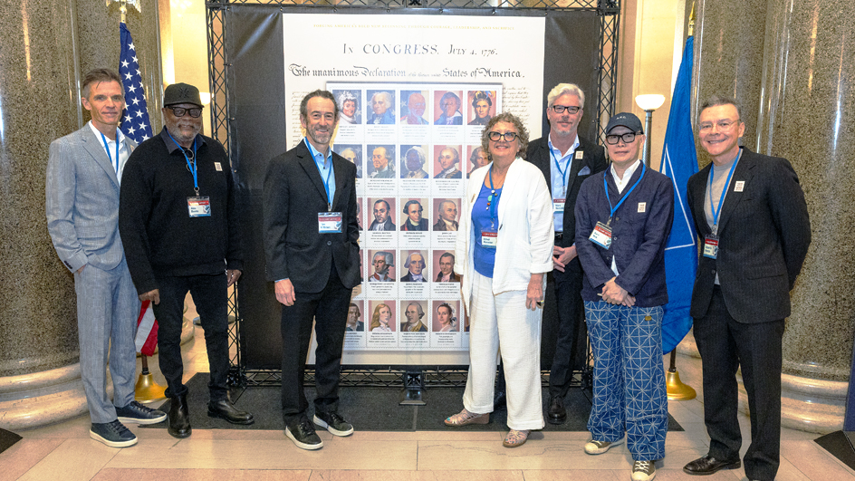 Group standing in front of a large display of Figures of the American Revolution stamps