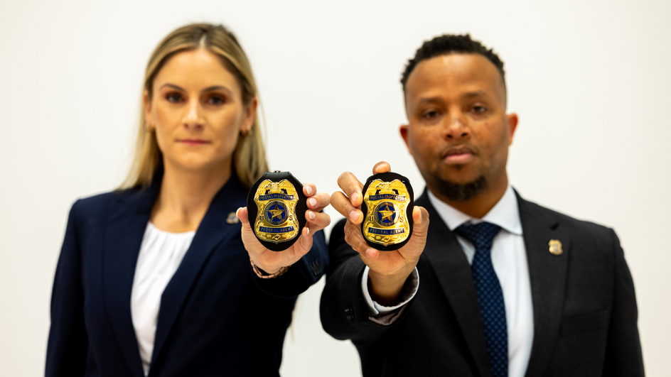 Two postal inspectors in formal attire holding up badges