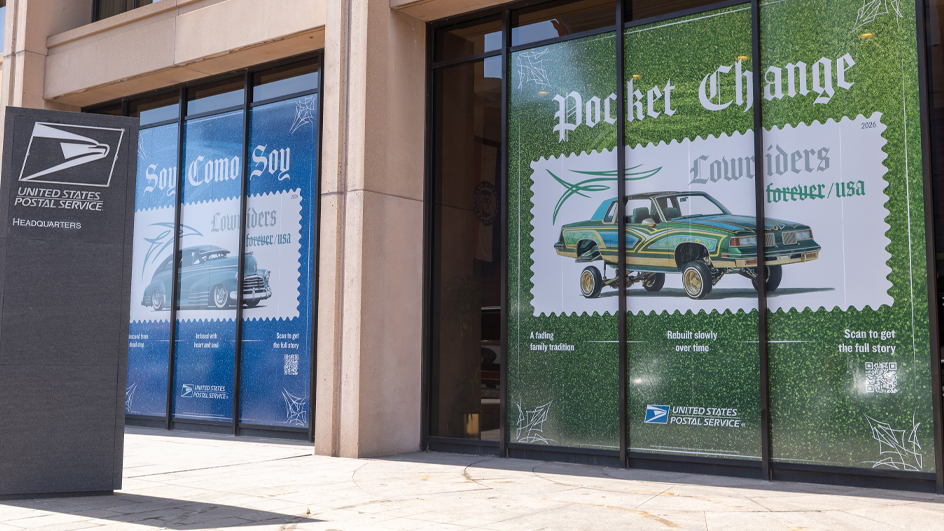 Large images of Lowriders stamps on a green and blue backgrounds filling up two large windows of a building.