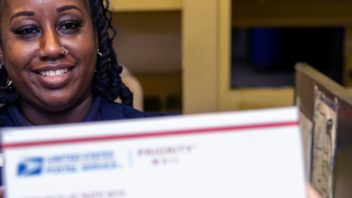 USPS employee holding out a Priority Mail box