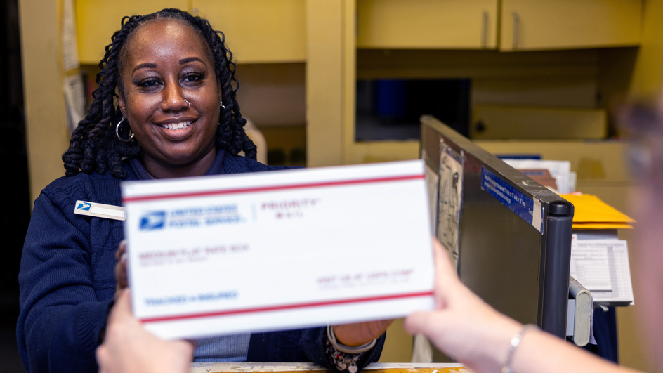 USPS employee holding out a Priority Mail box