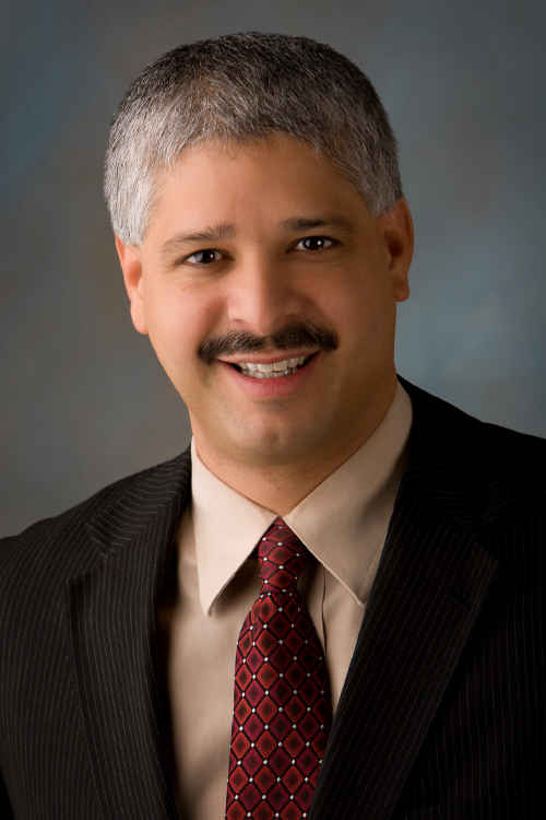Person in a suit with a patterned tie against a studio backdrop