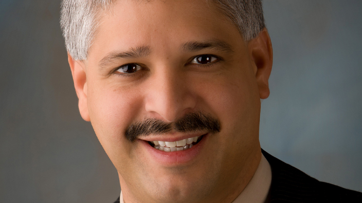 Person in a suit with a patterned tie against a studio backdrop