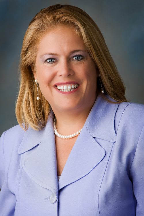 Person in a light-colored suit jacket wearing a pearl necklace.