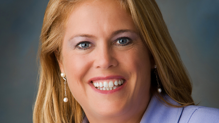 Person in a light-colored suit jacket wearing a pearl necklace.