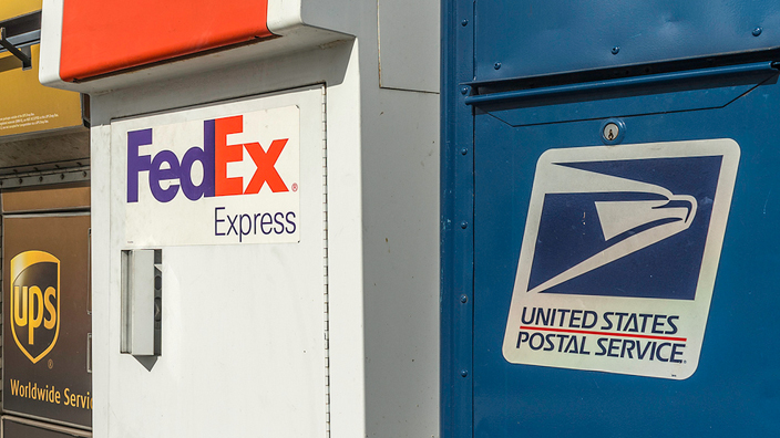UPS, FedEx and USPS delivery boxes on a street corner.