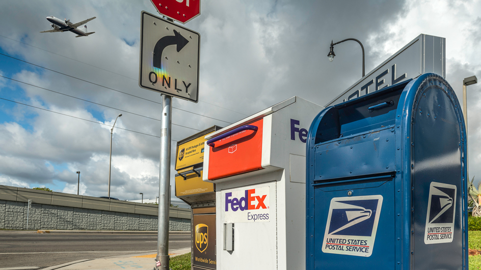 UPS, FedEx and USPS delivery boxes on a street corner.