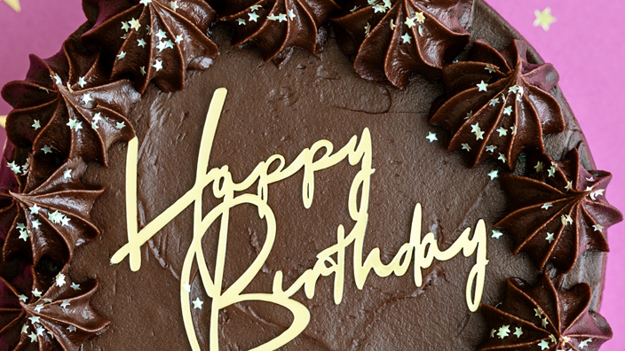 A chocolate-frosted cake with "Happy Birthday" written in yellow icing on top.