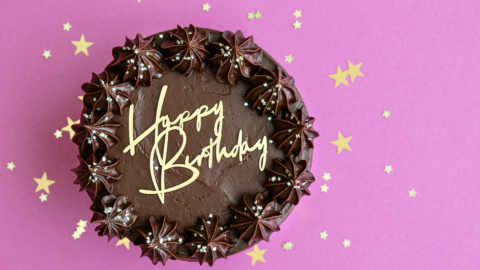A chocolate-frosted cake with "Happy Birthday" written in yellow icing on top.