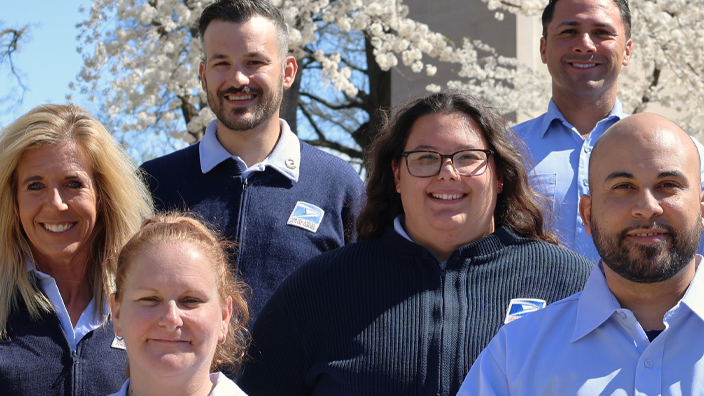 Group of postal employees standing outdoors in front of blooming trees.