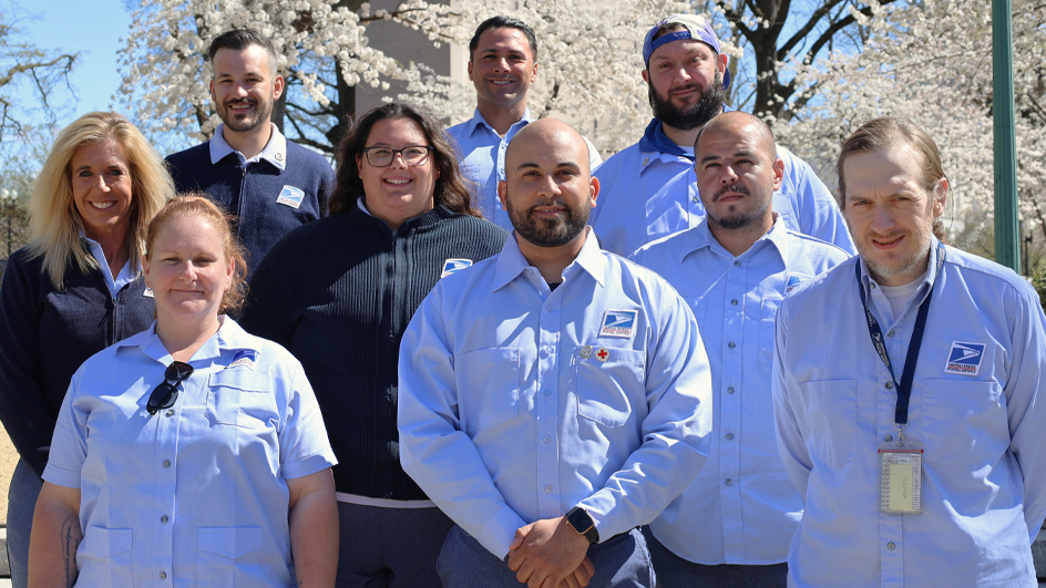 Group of postal employees standing outdoors in front of blooming trees.