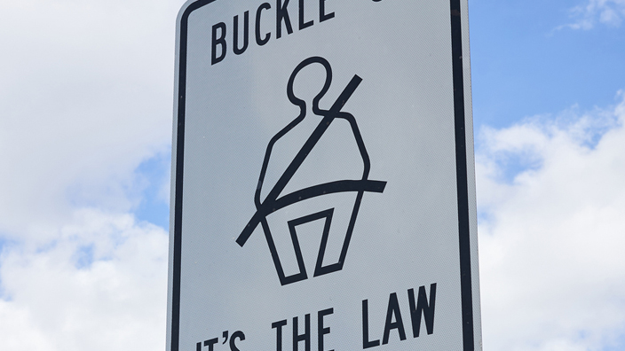 Buckle up sign and 'Click It or Ticket' warning sign against blue sky and clouds