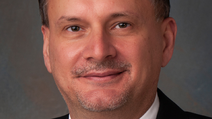 Portrait of a man wearing a dark suit, white shirt and patterned tie