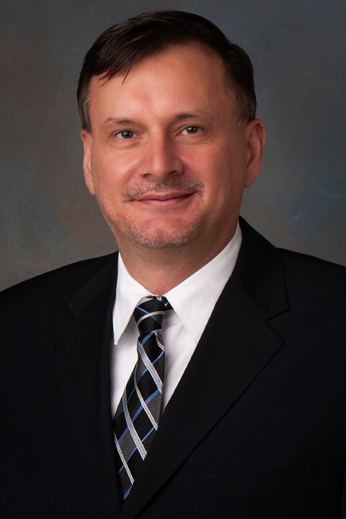 Portrait of a man wearing a dark suit, white shirt and patterned tie