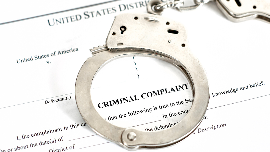 Handcuffs resting on a criminal complaint form from a U.S. District Court