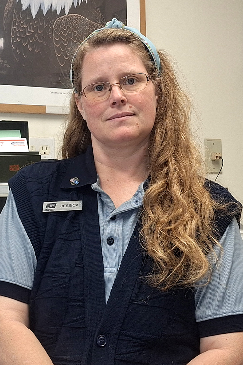 USPS employee wearing a light blue polo shirt underneath a dark blue sweater vest