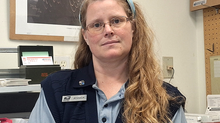 USPS employee wearing a light blue polo shirt underneath a dark blue sweater vest