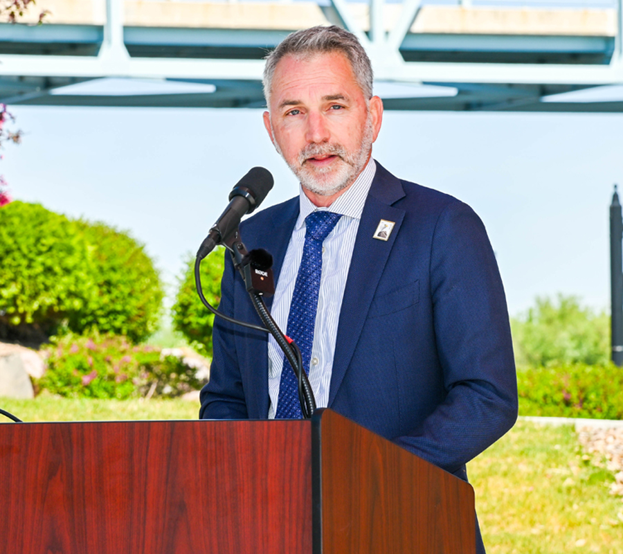 Man in a blue suit standing behind a podium and microphone outdoors