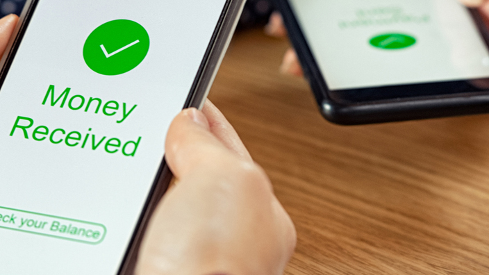 A pair of hands holding a cell phone with the words “money received” in green on the screen